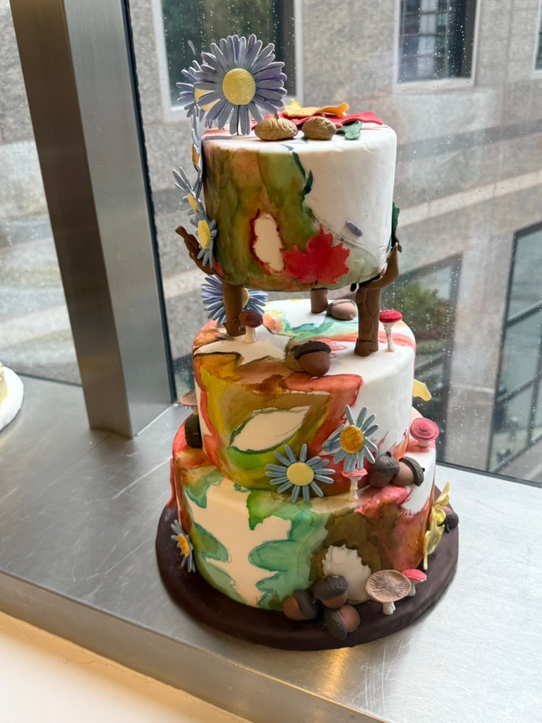 Colorful woodland-themed tiered cake created by a student chef