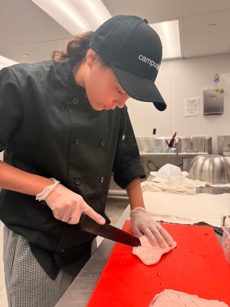Student chef practicing knife skills at a professional kitchen workstation